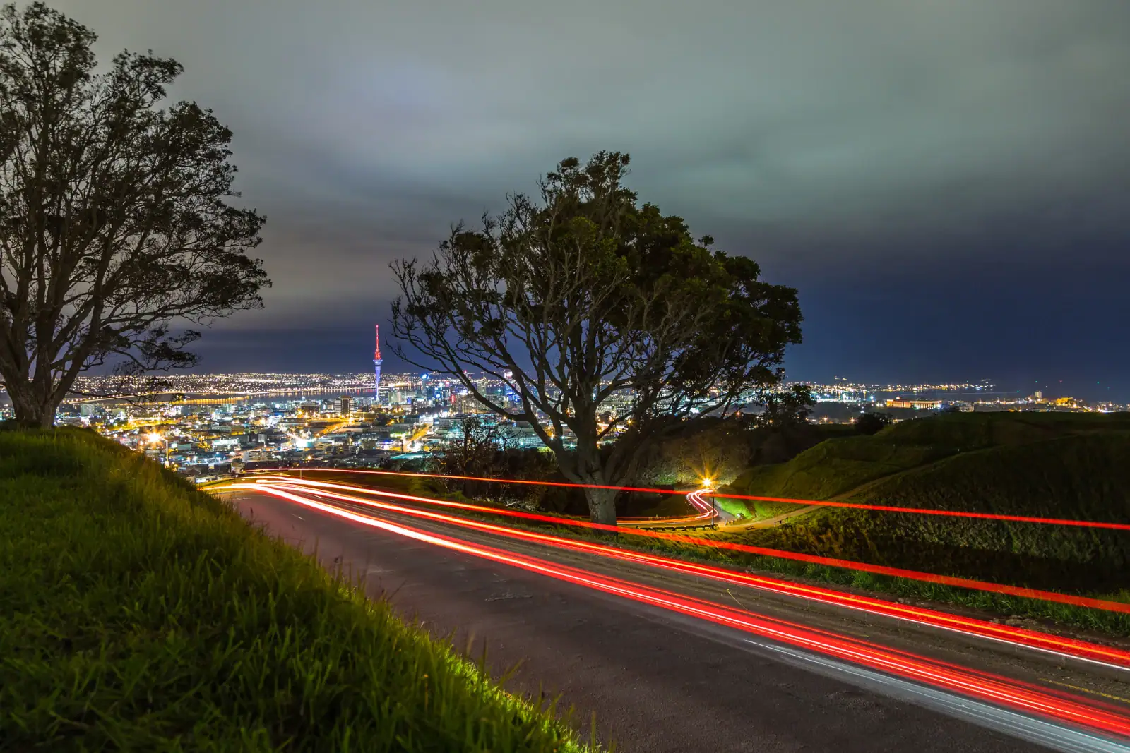 Auckland City at night seen from Mount Eden. Car light trails traveling in and out of the mountains car park.